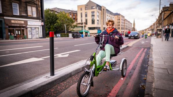 A woman rides a trike along a protected cycle lane beside a wide road in Edinburgh