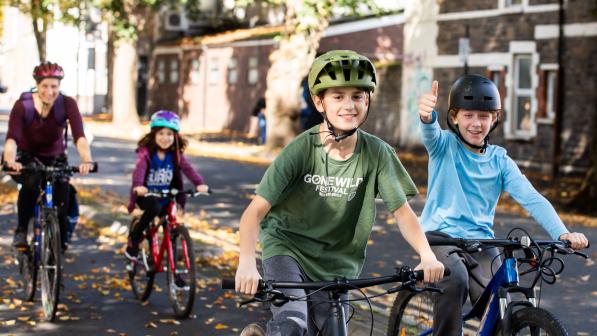 Two young boys are riding their bikes with a woman and a young girl cycling behind them, all on a segregated cycle lane. One of the boys is giving the camera a thumbs up