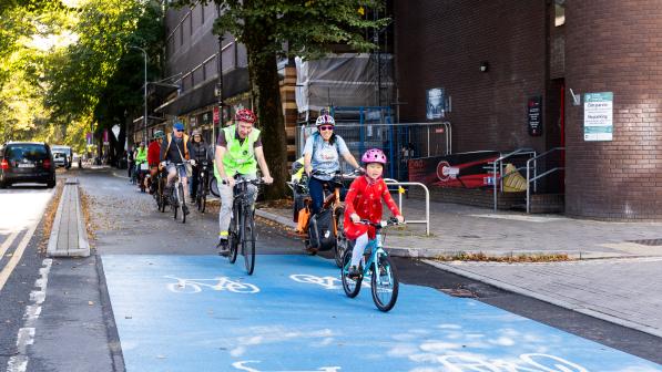 A  group of people is cycling along a protected cycle path with a child at the front of the group