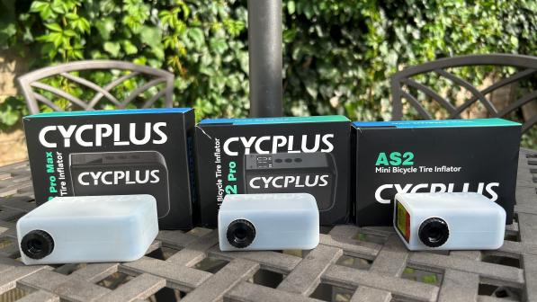 All three mini e-pumps are lined up next to their boxes on a table outside. A hedge is in the background