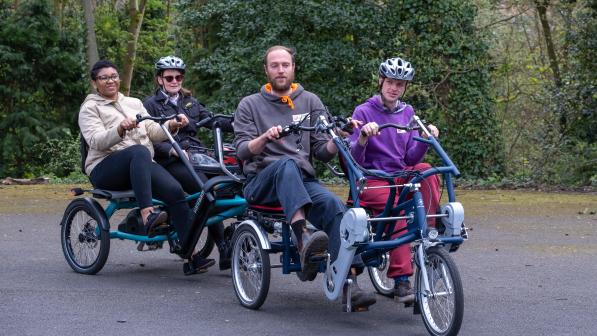 Four people on a non-standard cycle all peddling together on the pavement