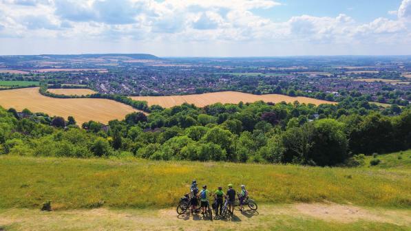 A group of people with bikes are standing together on the top of a mountain looking out over a valley