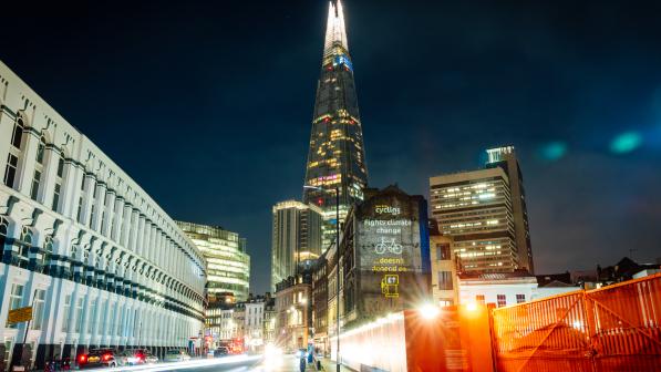 Projection in front of 'London's pyramid', the Shard building, with the words "Fights climate change" above a picture of a bike and "doesn't depend on" above a petrol pump