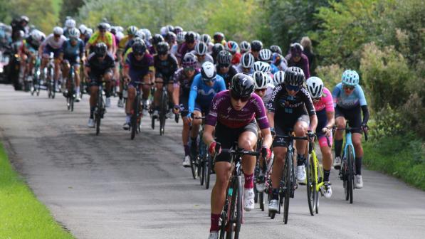 Demi Vollering cycling at a professional race. She is in currently leading with the rest of the peloton behind her.