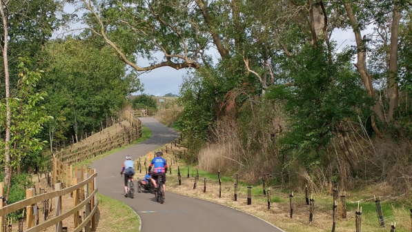 Two cyclists in the distance on a cycle path surrounded by green trees
