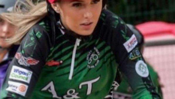 Emily Burgess riding, wearing a green and black racing jersey and pink helmet. Her facial expression is very focused..