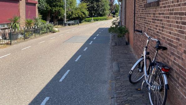 A Dutch-style bike is leaning against the brick wall of a house next to a single lane road 