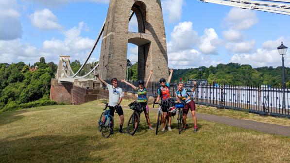 Four cyclists standing with their bikes next to the a bridge on their way to Glastonbury