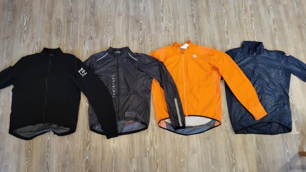 Four cycling jackets are lined up next to each other on a floor