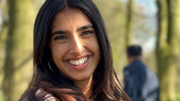 Hanna Ahmed is wearing a checked jacket and smiling as she is standing on a footpath surrounded by trees