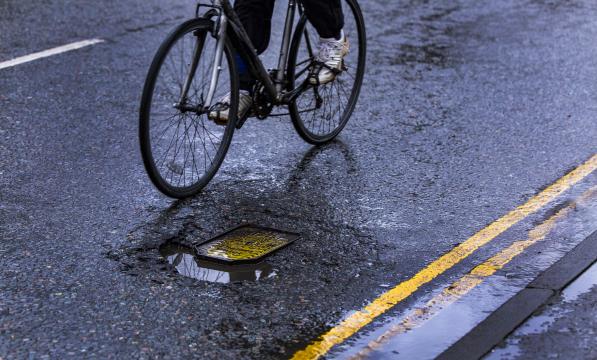 A person on a bicycle is riding around a pothole in the road