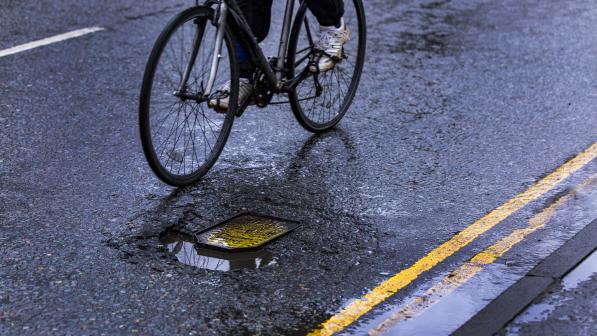 A person on a bicycle is riding around a pothole in the road