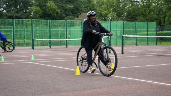 A woman wearing a helmet smiles as she confidently rides a bike through a cone course on a tennis court during a Big Bike Revival cycling session.