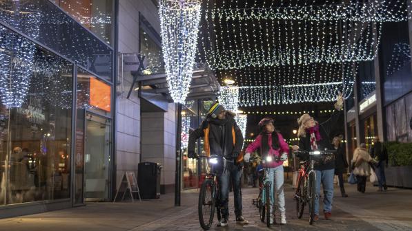 3 people walking with their bikes past Christmas lights © Joolze Dymond