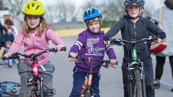 Three young children are standing astride bikes and smiling into the camera