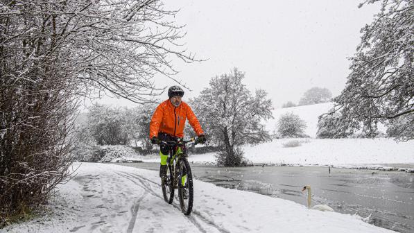 Man in a bright orange jacket is cycling on a mountain bike along a snowy track