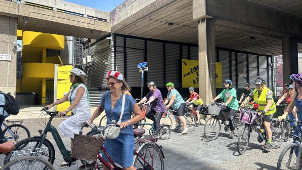 A big group of women are standing with their bikes looking ready to start cycling. They are all on different bikes and in normal clothes