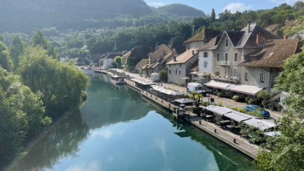 An attractive village on a river in mountains, with trees along the river and a road between the river and a row of pretty houses