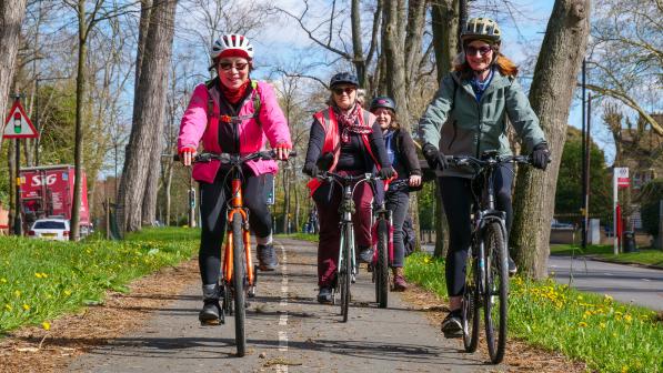 A group of four women are riding along a separated cycle lane. They're on hybrid bikes and wearing normal clothes. It's autumn so there are leaves on the ground and the women are wearing warm jackets