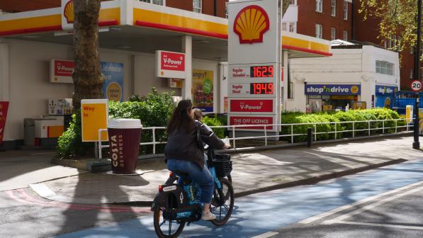 Cyclist cycling past a petrol station showing high prices for fuel