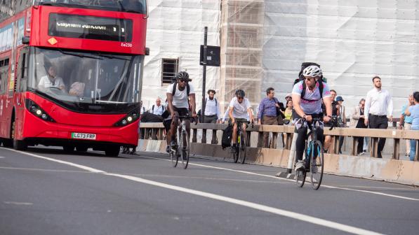 Two cyclists on a cycle and bus lane on London Bridge with a bus behind them