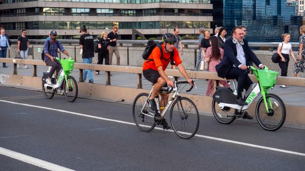 Three people are cycling on a separated cycle lane in an urban setting with people walking along the pavement in the background