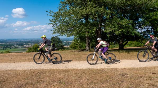 Three riders cycling along a gravel path, blue sky in the background. 