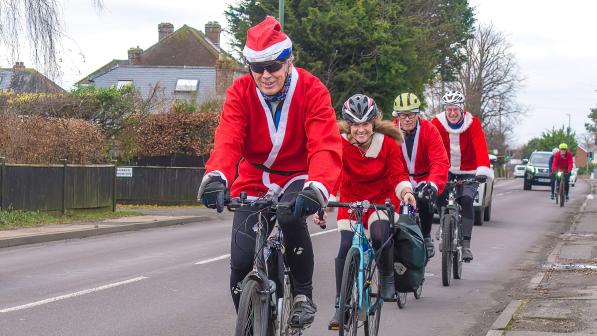 A group of people are cycling along a road all wearing Santa outfits