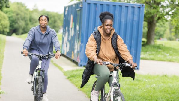 Two women cycling in a park smiling