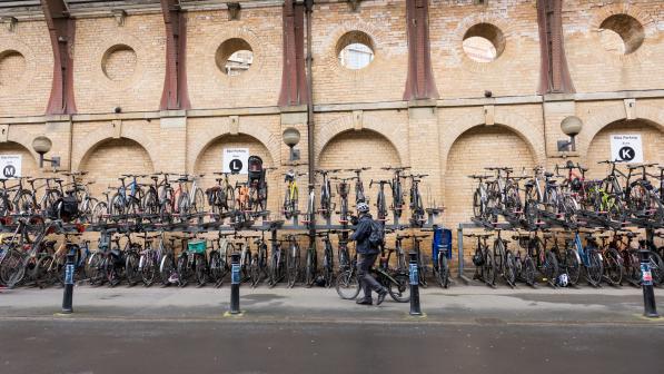 A person is wheeling a bike past several cycle racks with lots of bikes in them at a railway station