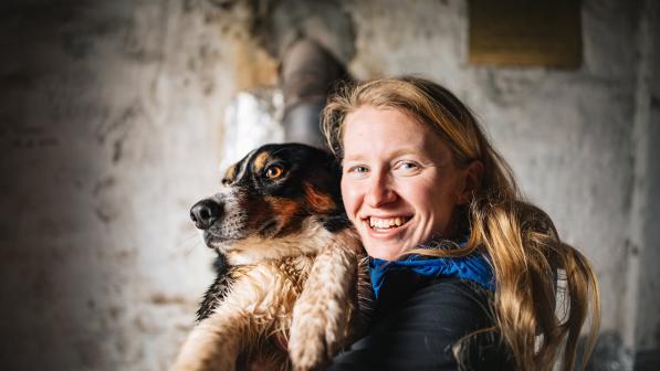 A headshot of Samantha Saskia Dugon. She has long blonde hair and is smiling into the camera. She’s holding a dog.