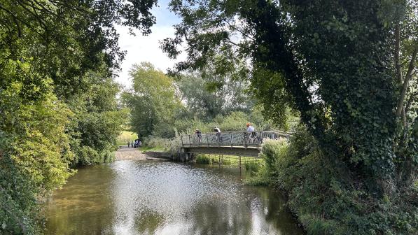 A wooden bridge over a stream with three people cycling over it