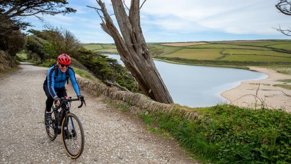 Man cycling in Cornwall on a gravel track with a lake to his left