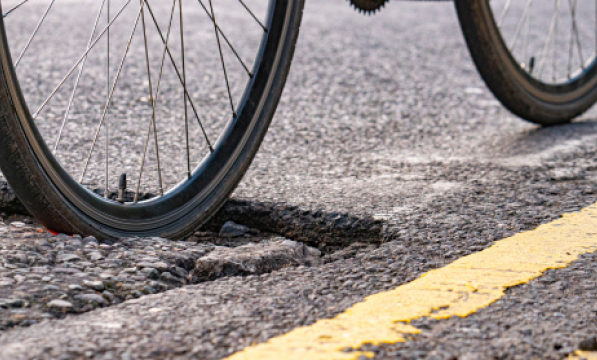 A bike wheel moving through a pothole in a road. 
