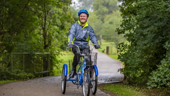 Man wearing a helmet cycling a trike outside on a footpath in a park