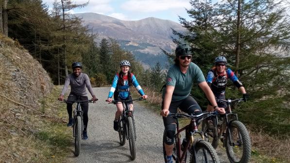 Four people are cycling along a gravel track. They're all on mountain bikes and wearing cycling kit and helmets