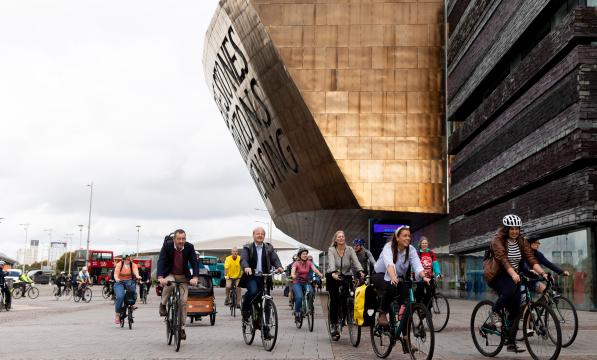 A large group of people are cycling round the Senedd building in Cardiff