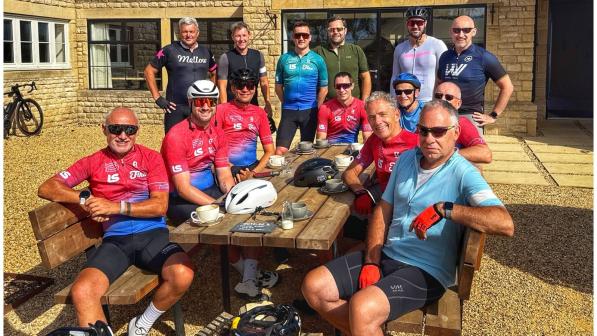 A group of men all wearing cycling kit is sitting at a wooden table