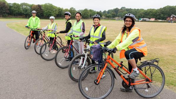 A group of people is on a tarmac path next to a field. They are all on bikes and look ready to set off on a ride