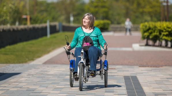 A women cycling a recumbent trike out in the sun on a pedestrianised path