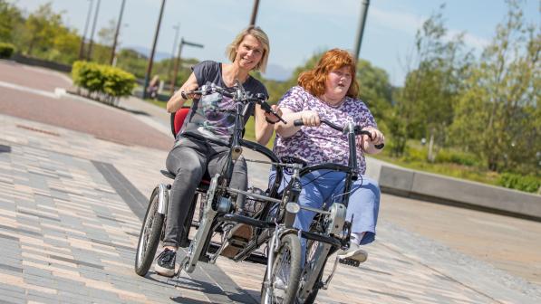Two people cycling outside on a path on a two seater trike