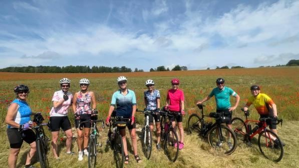A group of people holding bikes is standing in a field with a blue sky in the background