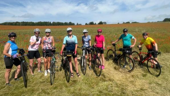 A group of people holding bikes is standing in a field with a blue sky in the background