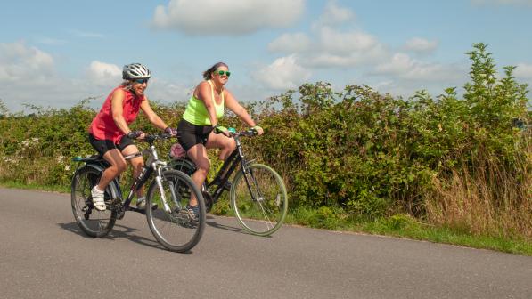 Two women cycling on the road in the sun