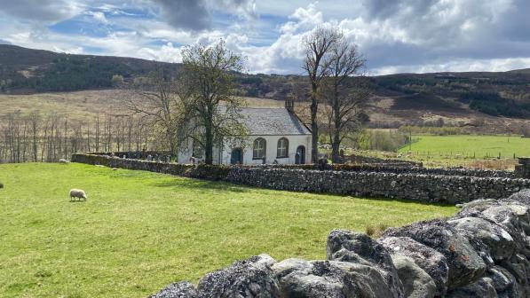 A church in a field, surrounded by dry stone walls and trees