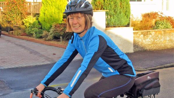 A woman is riding a black touring bike. She's wearing cycling kit and a helmet