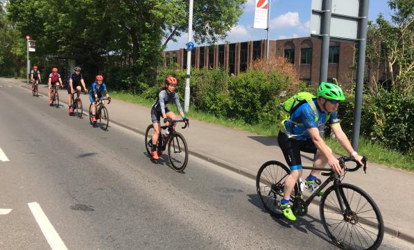 Six cyclists are riding along an urban road in single file