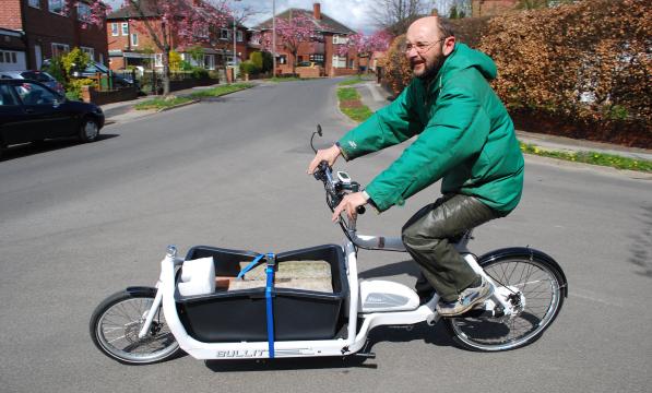 A man in a green puffa jacket and green trousers is riding a white e-cargo bike carrying 110kg of concrete