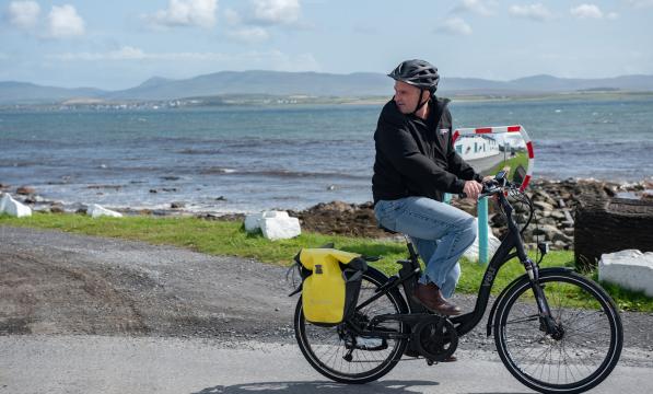 A cyclist on an ebike, carrying panniers along a coastal road. 
