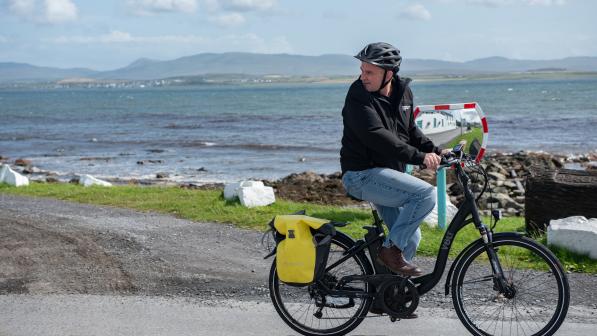 A cyclist on an ebike, carrying panniers along a coastal road. 